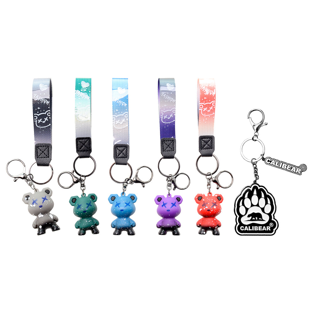 Five Calibear collectible streetwear bear keychain figurines in black, green, blue, purple, and red alongside a premium black and silver metal Calibear bear paw logo keychain.