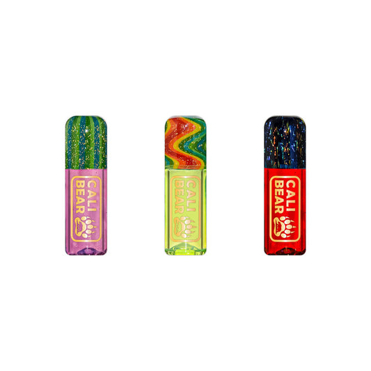 Three Calibear premium reusable glass filter tips shown side-by-side with gold logos, featuring a pink base with a green dichro top, a lime green base with a rainbow wigwag top, and a red base with a dark shimmering dichro top.